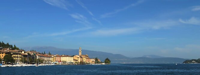 Trip Italien beliebte Urlaubsziele am Gardasee -  Mit einer Fläche von 370 km² ist der Gardasee der größte See Italiens. Es liegt am Fuße der Alpen und erstreckt sich über drei Staaten: Lombardei, Venetien und Trentino. Die maximale Tiefe des Sees beträgt 346 m, er hat eine längliche Form und sein nördliches Ende ist sehr schmal. Dort ist der See von den Bergen der Gruppo di Baldo umgeben. Du trittst aus deinem gemütlichen Hotelzimmer und es begrüßt dich die warme italienische Sonne. Du blickst auf den atemberaubenden Gardasee, der in zahlreichen Blautönen schimmert - von tiefem Dunkelblau bis zu funkelndem Türkis. Majestätische Berge umgeben dich, während die Brise sanft deine Haut streichelt und der Duft von blühenden Zitronenbäumen deine Nase kitzelt. Du schlenderst die malerischen, engen Gassen entlang, vorbei an farbenfrohen, blumengeschmückten Häusern. Vereinzelt unterbricht das fröhliche Lachen der Einheimischen die friedvolle Stille. Du fühlst dich wie in einem Traum, der nicht enden will. Jeder Schritt führt dich zu neuen Entdeckungen und Abenteuern. Du probierst die köstliche italienische Küche mit ihren frischen Zutaten und verführerischen Aromen. Die Sonne geht langsam unter und taucht den Himmel in ein leuchtendes Orange-rot - ein spektakulärer Anblick.